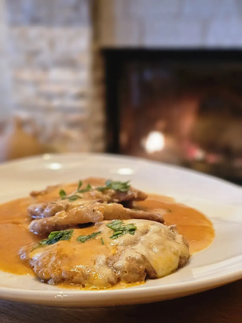 Meat in sauce with melted cheese, a lit fireplace behind