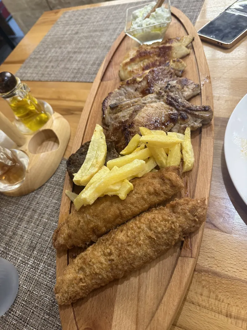 A wooden board with grilled meat, fried fish and fries