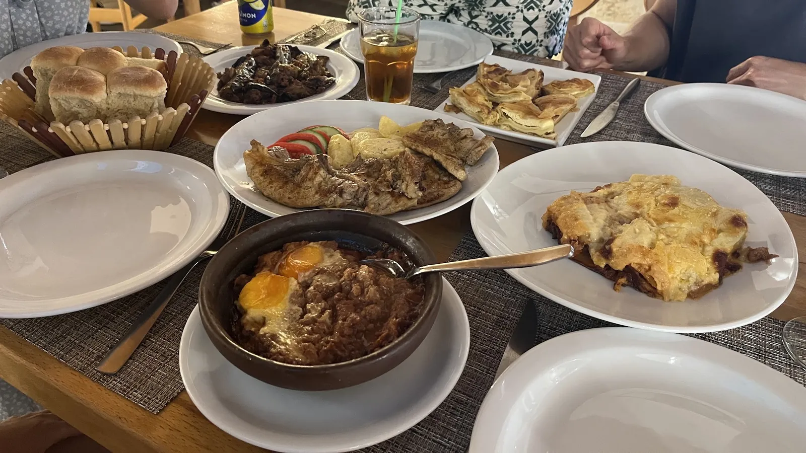 A table full of moussaka, kima with eggs in a clay pot, byrek, grilled meat and bread