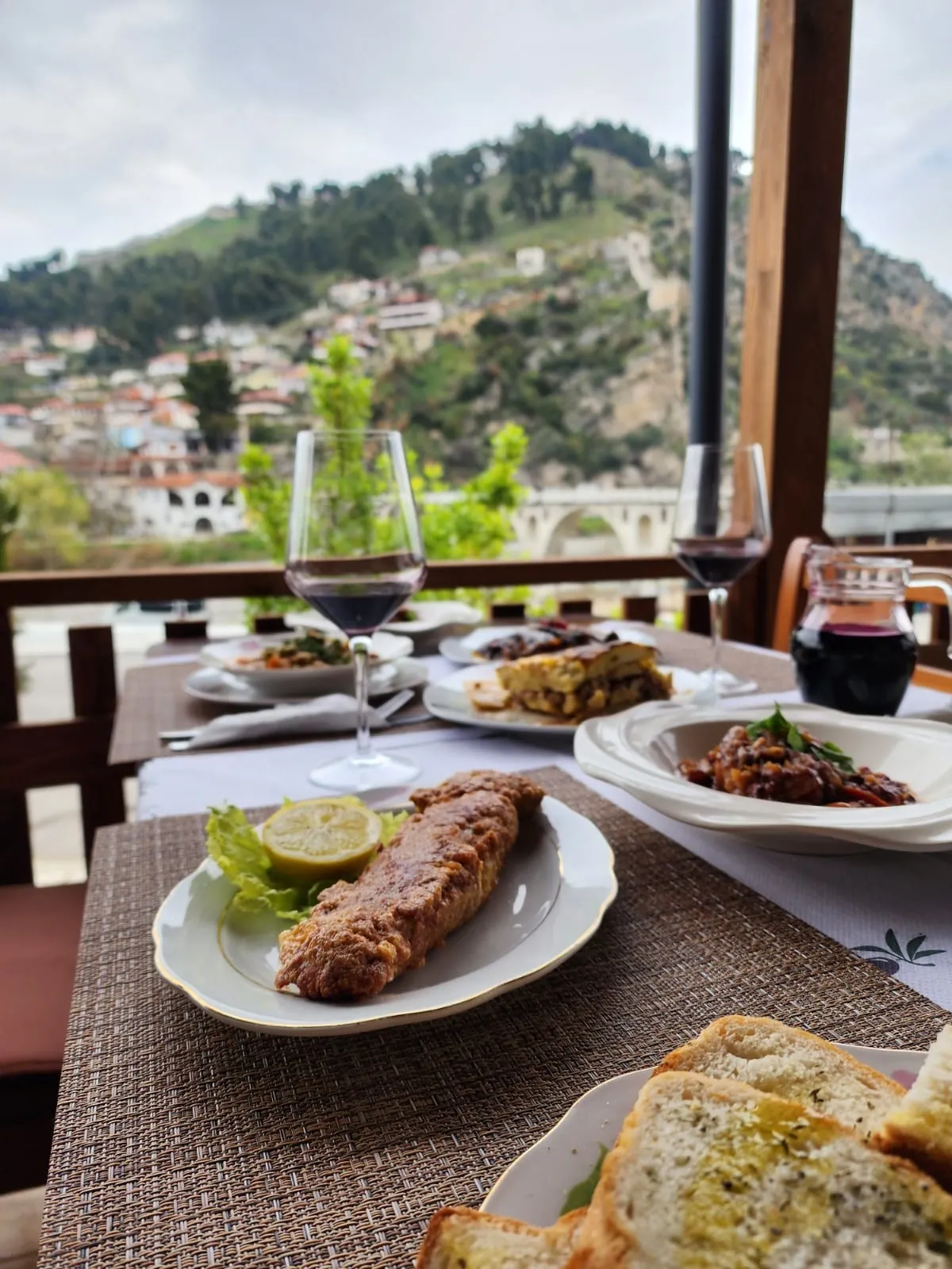 A terrace table with moussaka and red wine, looking out at Berat castle hill