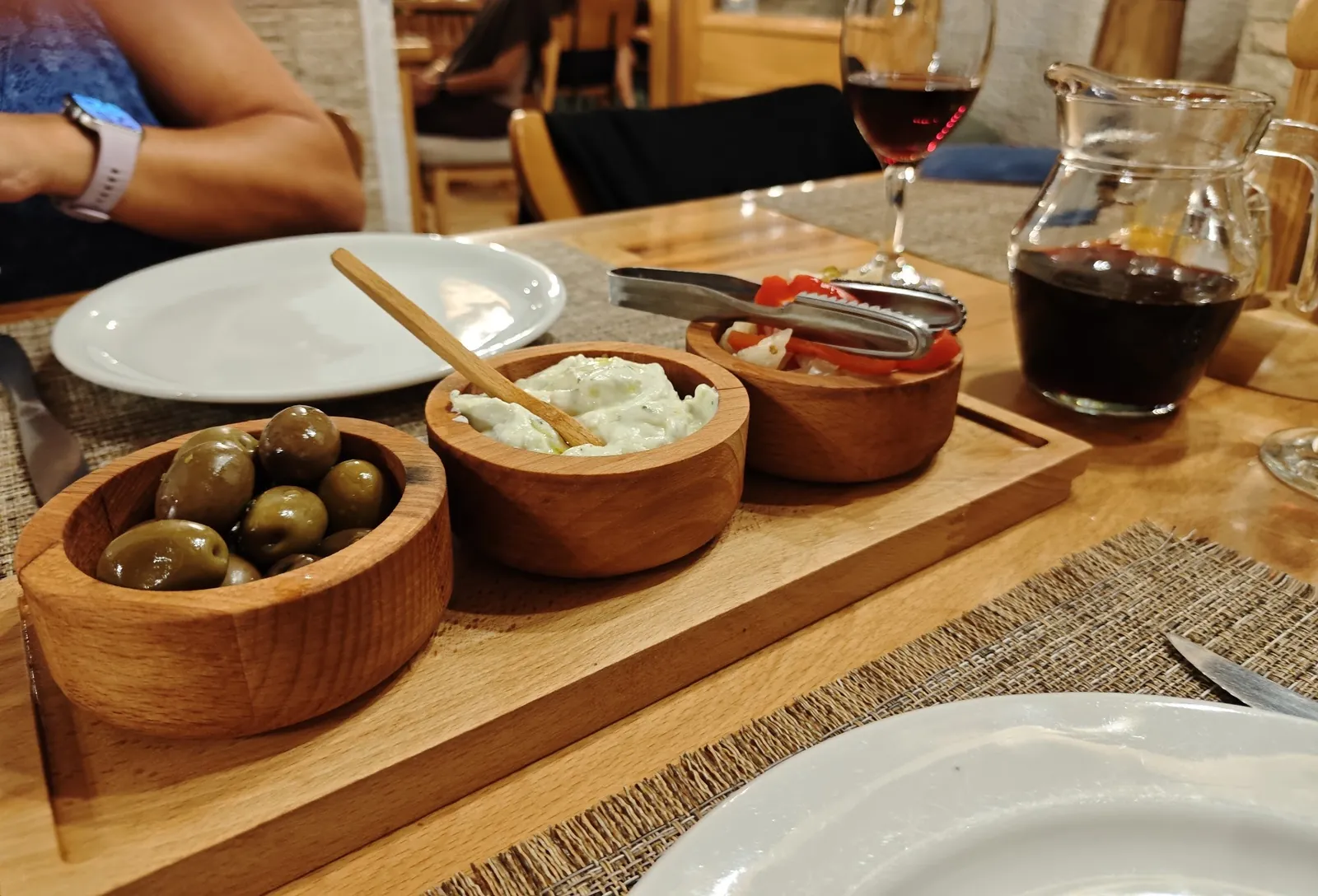 Olives, cream and peppers in wooden bowls next to a carafe of red wine
